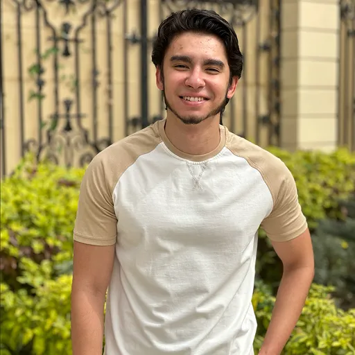 Mostafa Abdelsalam smiling in a cream raglan tee in front of an iron gate